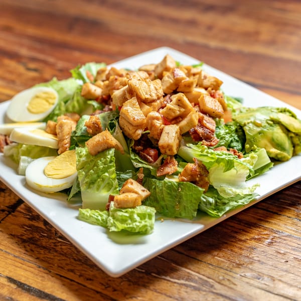 Oy! breakfast salad with chicken, avocado, bacon, hard-boiled eggs, and lettuce on a white plate.