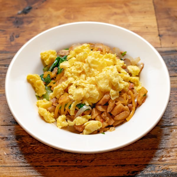 A white plate of scrambled eggs, breakfast potatoes, onions, and spinach on a wooden table.