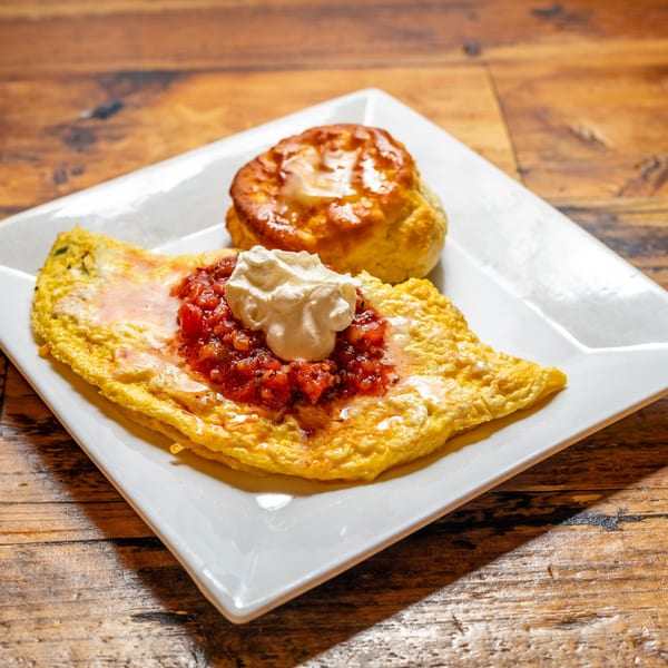 A breakfast omelet topped with salsa and sour cream, served with a biscuit on a white plate.