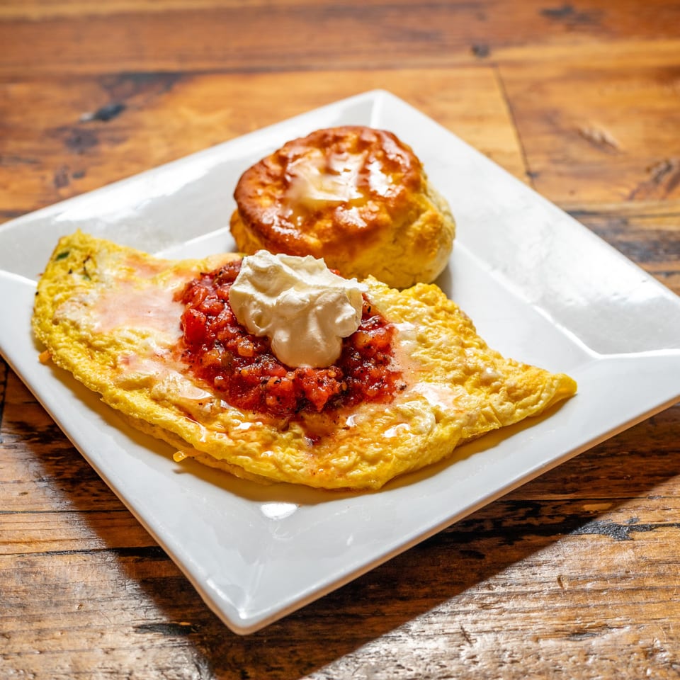 A breakfast omelet topped with salsa and sour cream, served with a biscuit on a white plate.